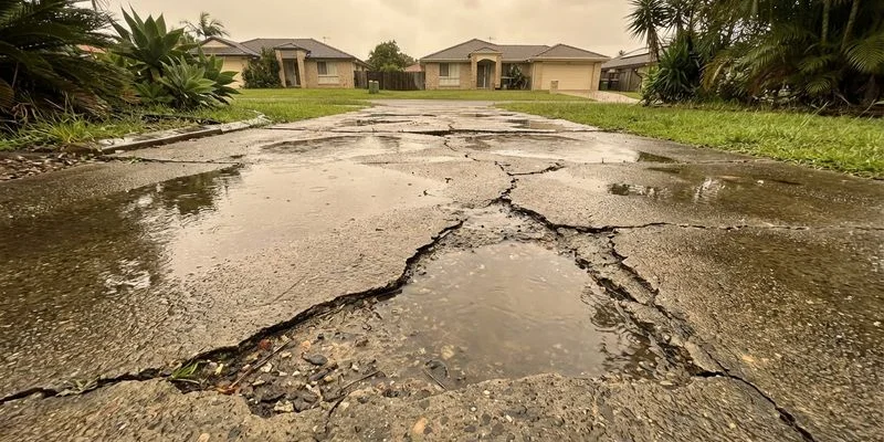 Water pooling on an uneven concrete driveway surface after heavy rainfall showing poor drainage and surface deterioration